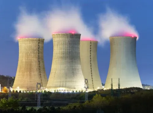 Torri di raffreddamento di una centrale nucleare illuminate al crepuscolo, con vapore e tralicci dell’alta tensione. Immagine di apertura dell’articolo sulla corsa delle Big Tech agli accordi energetici per alimentare i data center dell’intelligenza artificiale.