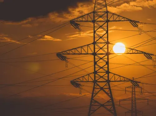 Tralicci dell'alta tensione in controluce al tramonto, con il sole tra i cavi elettrici