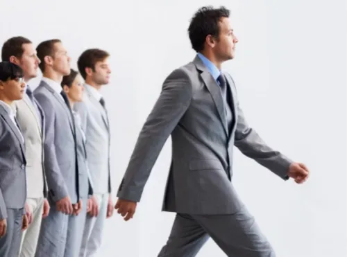 Gruppo di professionisti in abito grigio allineati; uno di loro avanza deciso davanti agli altri, che restano fermi